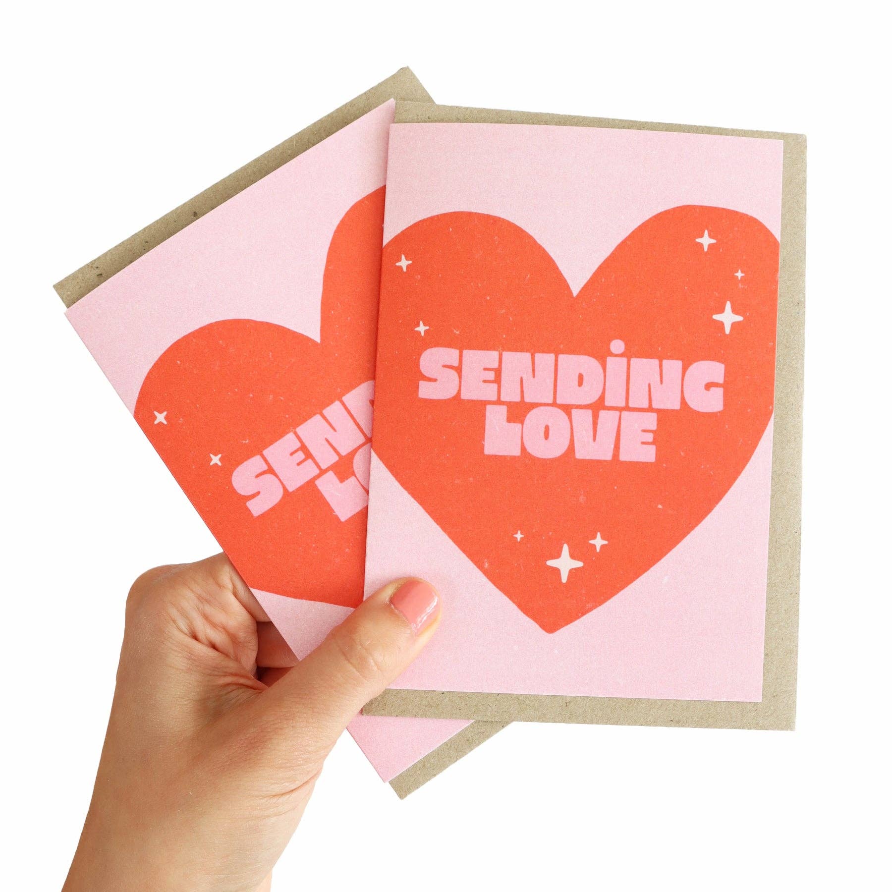 Hand holding a card with a red heart and 'Sending Love' text on a pink background